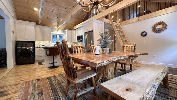 A rustic kitchen with a wooden table and chairs, a washing machine, and a Christmas tree.