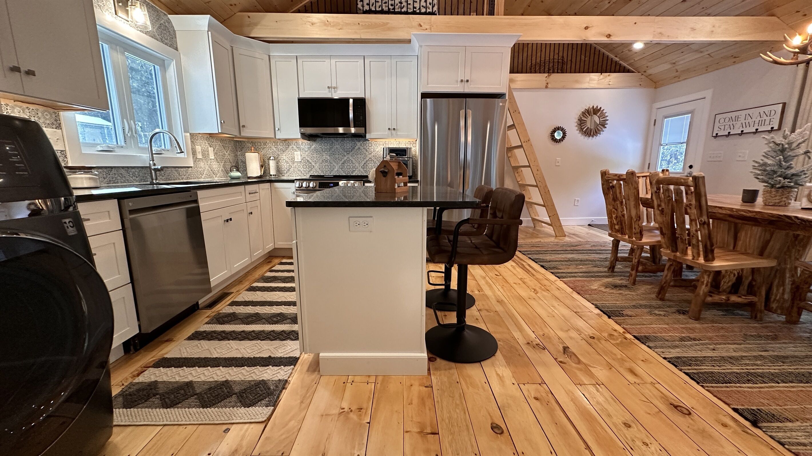 Een moderne keuken met witte kastjes, een roestvrijstalen koelkast en een eethoek met een houten vloer en rustieke stoelen.