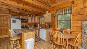 Cocina de cabaña de madera con una isla central, sillas de madera, un refrigerador, un microondas y un lavamanos.