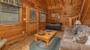 Interior acogedor de una cabaña de madera con suelo de madera, un sofá, una mesa de centro y una lámpara.