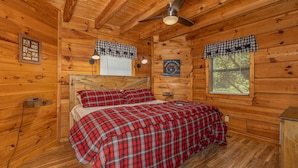 Un dormitorio de cabaña de madera con una cama, un ventilador de techo y una ventana con persianas.