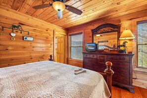 Habitación de cabaña de madera con cama, cómoda, televisor y ventilador de techo.