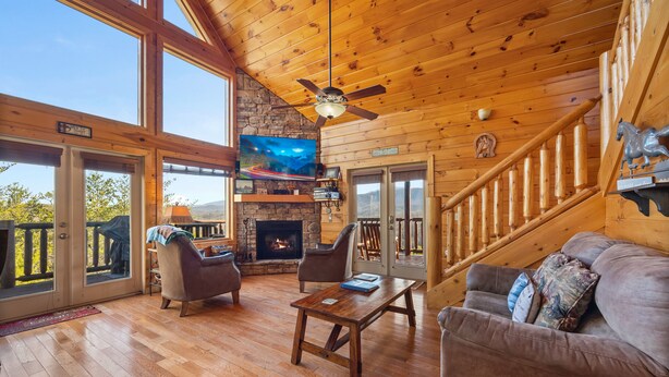 A spacious living room with a fireplace, wooden ceiling, and a large TV. - Galloping In The Mountains (PIGEON FORGE)