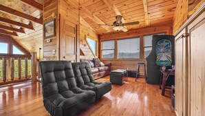 A spacious room with wooden floors, a ceiling fan, a sofa, a coffee table, and a large window with blinds. - Galloping In The Mountains (PIGEON FORGE)