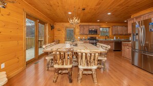 A log cabin kitchen with wooden walls, a central island table, and a stainless steel refrigerator. - Retreat To The Mountain Lair (SEVIERVILLE)