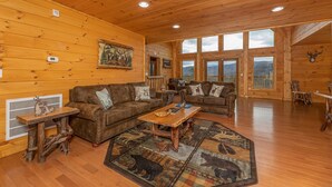 A log cabin interior with wooden walls, a large window, a fireplace, and a cozy seating area. - Retreat To The Mountain Lair (SEVIERVILLE)