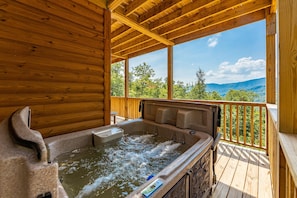 Una cabaña de madera con jacuzzi y terraza de madera con vistas a un paisaje montañoso.