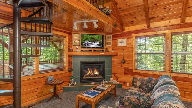 A cozy cabin interior with a fireplace, a television, a sofa, and a spiral staircase. - The Perfect Couple’s Retreat (PIGEON FORGE)