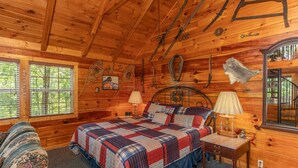A wooden cabin bedroom with a bed, a nightstand, a lamp, and a window. - The Perfect Couple’s Retreat (PIGEON FORGE)