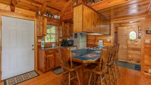 A wooden cabin interior with a kitchen, dining area, and a door. - The Perfect Couple’s Retreat (PIGEON FORGE)