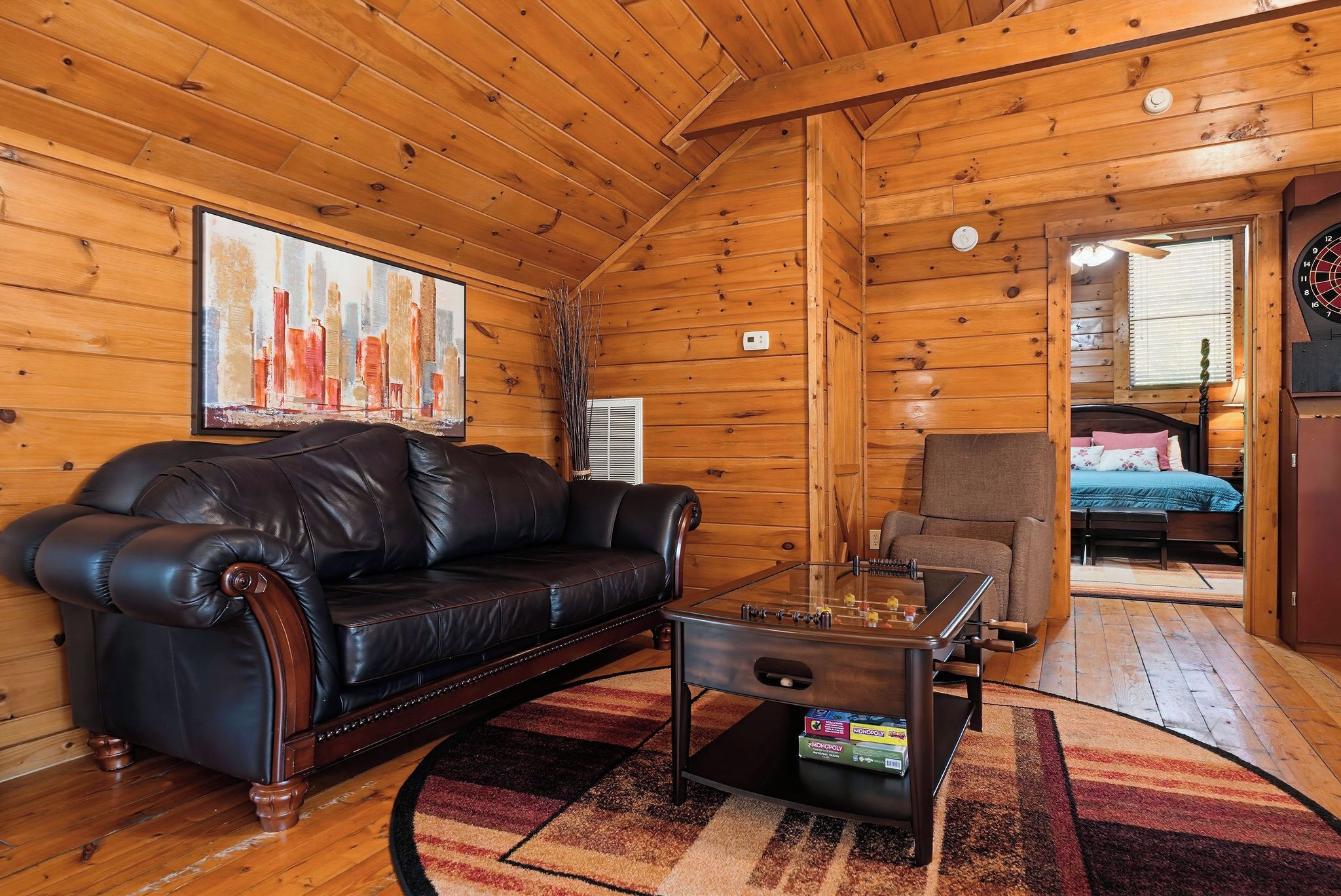 A cozy cabin interior with a leather sofa, a coffee table with board games, and a wooden ceiling.