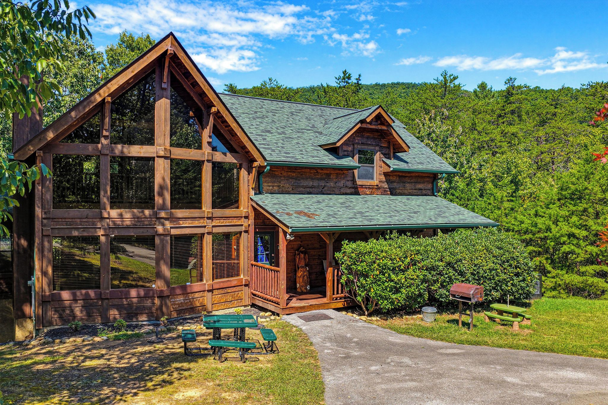 A log cabin with a large porch, a covered entryway, and a small front yard with a bench and mailbox.