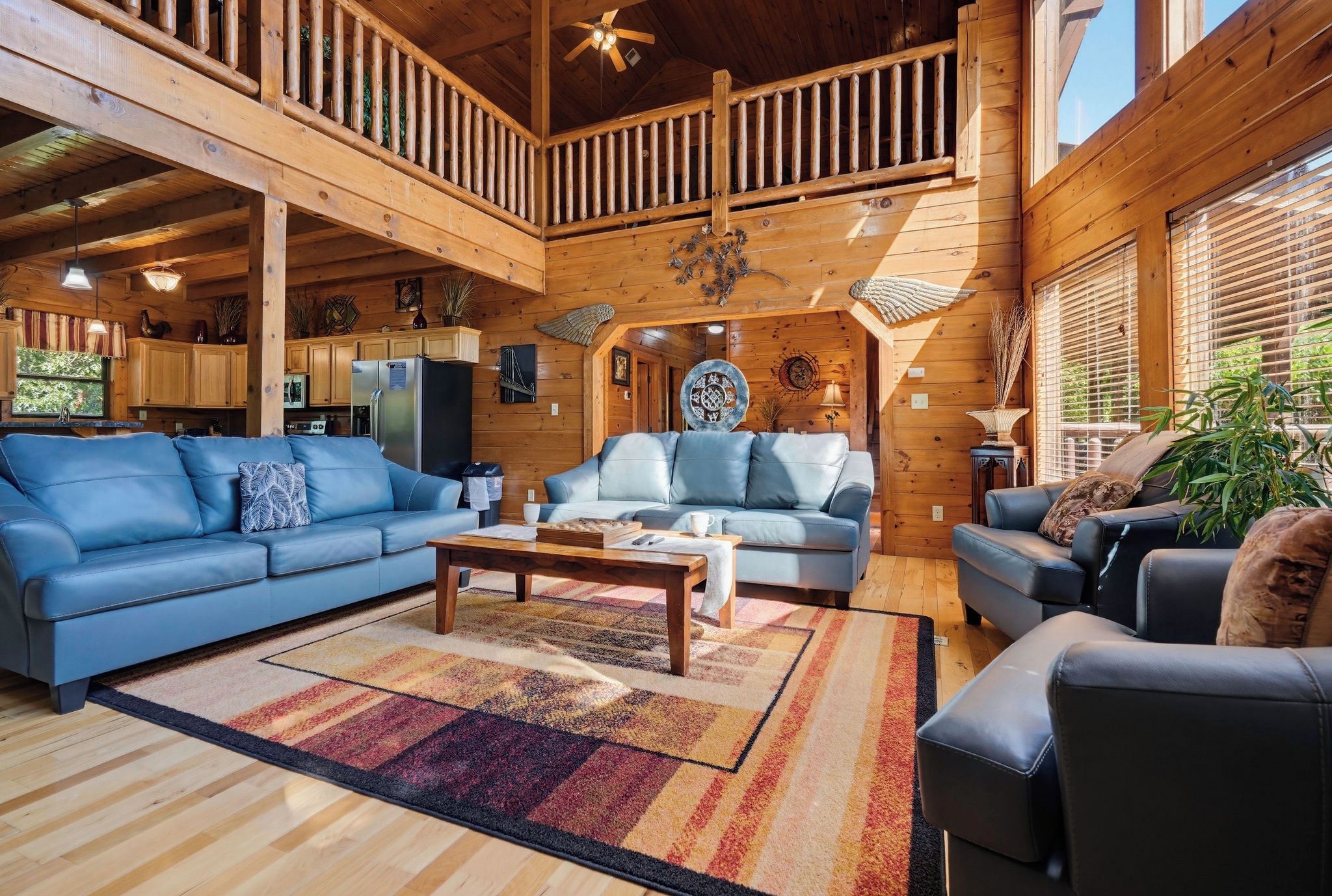 A spacious living area with a high ceiling, wooden beams, a kitchen in the background, and a large window with blinds.