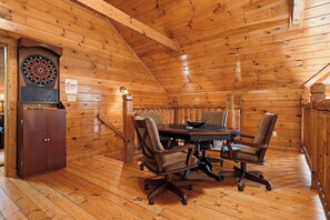 A wooden interior with a dartboard, a table, and four chairs.