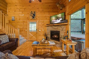 Un interior de cabaña acogedor, con chimenea de piedra, paredes de madera, un sofá cómodo y un televisor.