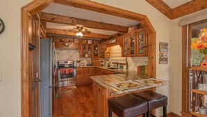 A kitchen with wooden beams, a refrigerator, a stove, and a bar area with stools. - Pigeon Forge*Easy Access Rds*WiFi*Hot Tub (SEVIERVILLE)