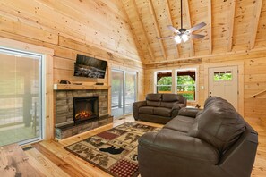 Ein gemütliches Blockhaus-Interieur mit Kamin aus Stein, einer Ledersofa und einem Deckenventilator.