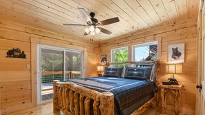 A wooden cabin bedroom with a bed, a ceiling fan, and a window. - Close to Pigeon Forge*Keurig*Hot Tub (PIGEON FORGE)