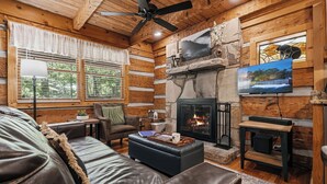 A log cabin interior with a fireplace, a television, leather furniture, and a stone accent wall. - Secluded*Enclosed Hot Tub*Cozy (PIGEON FORGE)