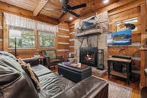 A log cabin interior with a fireplace, a television, leather furniture, and a stone accent wall.