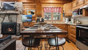 A cozy kitchen with wooden cabinets, a stone fireplace, a dining table set for four, and a modern microwave. - Secluded*Enclosed Hot Tub*Cozy (PIGEON FORGE)