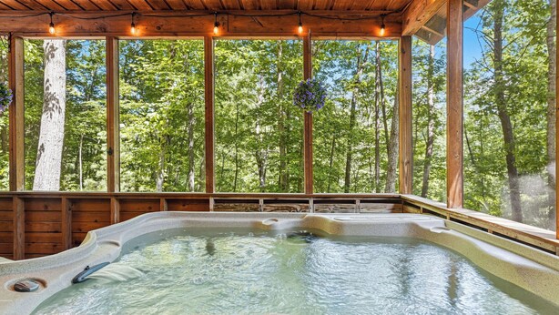 A hot tub in a wooden cabin with large windows and a forest view. - Secluded*Enclosed Hot Tub*Cozy (PIGEON FORGE)