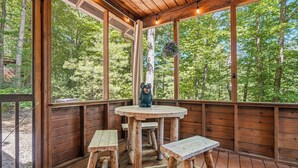 A wooden deck with a table and benches, large windows, and a hanging flower basket. - Secluded*Enclosed Hot Tub*Cozy (PIGEON FORGE)