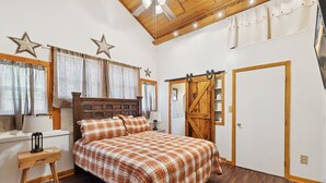 A bedroom with a wooden bed, a nightstand, a dresser, a sliding barn door, and a ceiling fan.