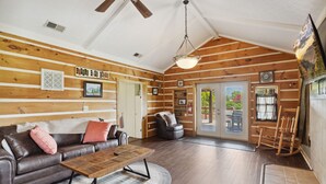 A log cabin interior with a leather sofa, wooden coffee table, and a ceiling fan.