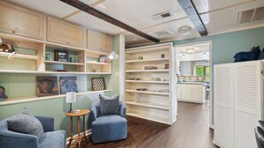 A room with a wooden floor, a blue armchair, a small table with a lamp, and a bookshelf.