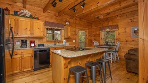 A wooden cabin interior with a kitchen featuring granite countertops, wooden cabinets, a dishwasher, and a dining area with a table and chairs. - Simplicity Like It Should Be: In A Cabin (PIGEON FORGE)