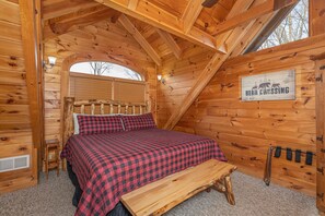 Acogedor dormitorio de cabaña de madera con cama, banca y un cartel que indica paso de osos.