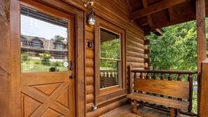 A wooden cabin with a large door, a bench, and a window overlooking a garden. - Unplug And Unwind In A Pigeon Forge Luxury Cabin (PIGEON FORGE)
