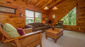 A cozy cabin interior with a wooden ceiling, a sofa, a wicker chair, a small table, and a window offering a view of the outdoors. - Unplug And Unwind In A Pigeon Forge Luxury Cabin (PIGEON FORGE)