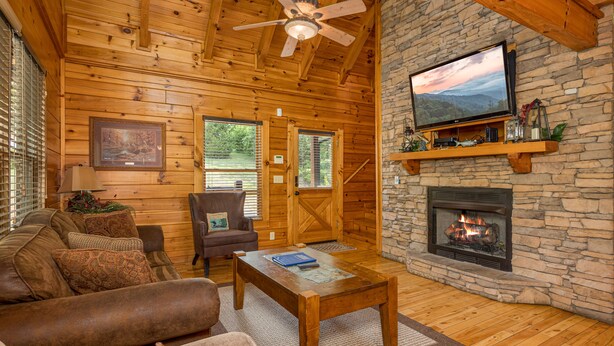 A cozy log cabin interior with a stone fireplace, wooden ceiling, and a television mounted above it. - Unplug And Unwind In A Pigeon Forge Luxury Cabin (PIGEON FORGE)