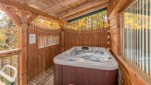 Uma cabana de madeira com banheira de hidromassagem, deck de madeira e vista para árvores de outono.