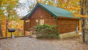 Uma cabana rústica com telhado verde, rodeada por folhagem de outono.