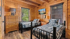A cabin-style room with two beds, a dresser, a television, and a window with blinds. - Filling Your Vacation Time With Fun And Games (PIGEON FORGE)