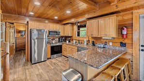 A wooden cabin-style kitchen with granite countertops, stainless steel appliances, and wooden cabinets. - Filling Your Vacation Time With Fun And Games (PIGEON FORGE)