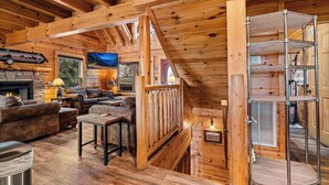 A cozy log cabin interior with a fireplace, wooden furniture, and a metal shelf unit. - Filling Your Vacation Time With Fun And Games (PIGEON FORGE)