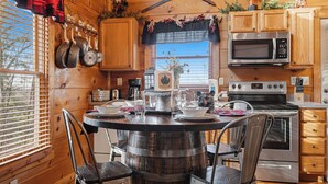 A wooden cabin interior with a round wooden table, chairs, a stove, a microwave, and a window with blinds. - Relax And Enjoy The Incredible View From Here (GATLINBURG)