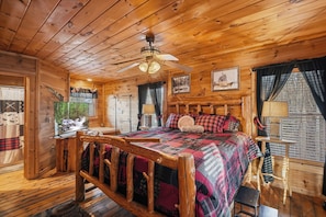 Ein Holzblockhaus-Interieur mit Bett, Deckenventilator und rustikalen Einrichtungsgegenständen.