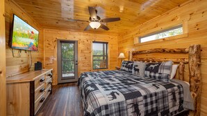 Une chambre dans un chalet en bois, avec un lit, un ventilateur de plafond, une télévision et une fenêtre.