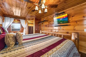 A wooden cabin room with a bed, curtains, a television, and a ceiling fan. - Nothing Sweeter Than Views Like These (SEVIERVILLE)