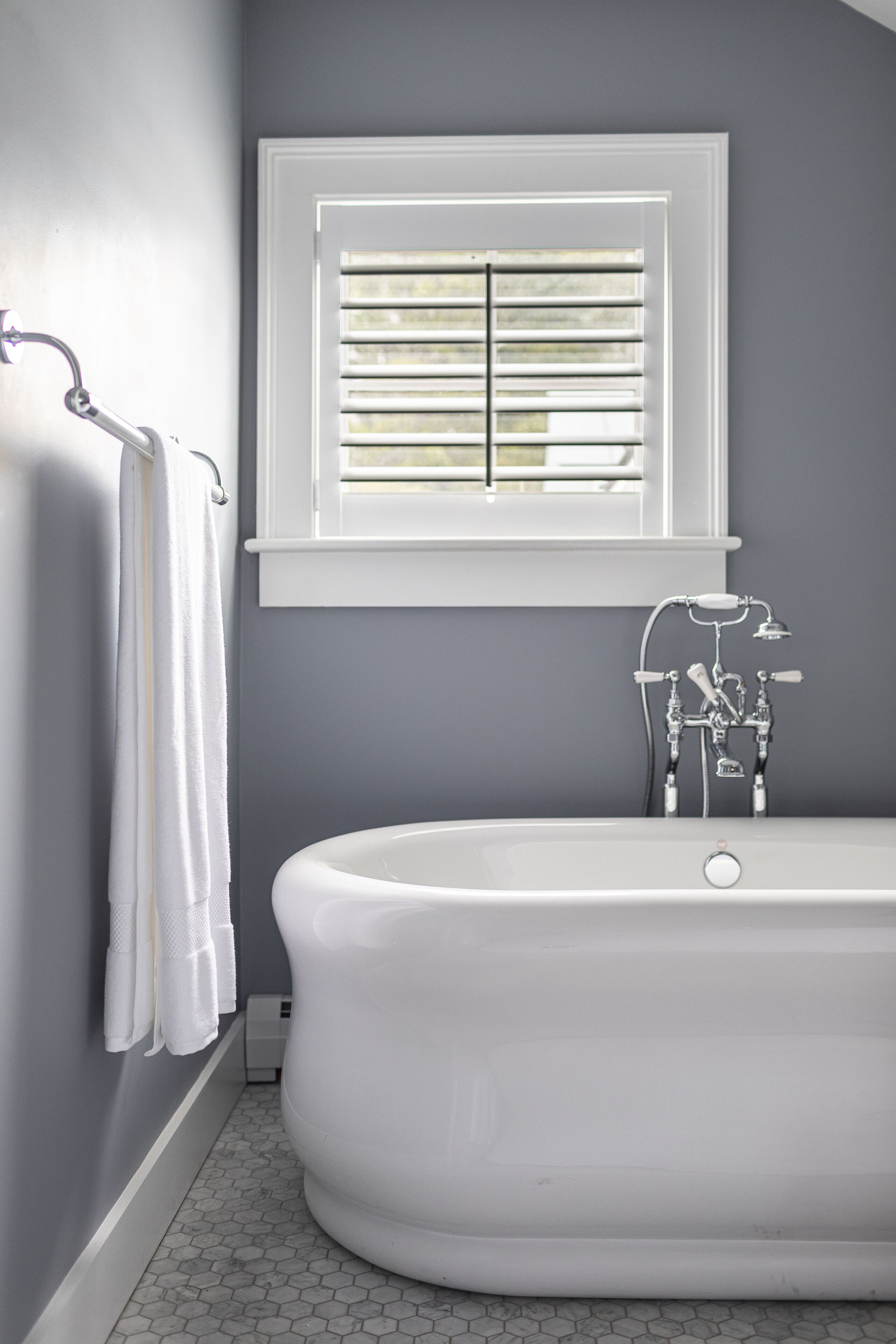 A bathroom with a freestanding bathtub, a window with blinds, and a towel rack with white towels.
