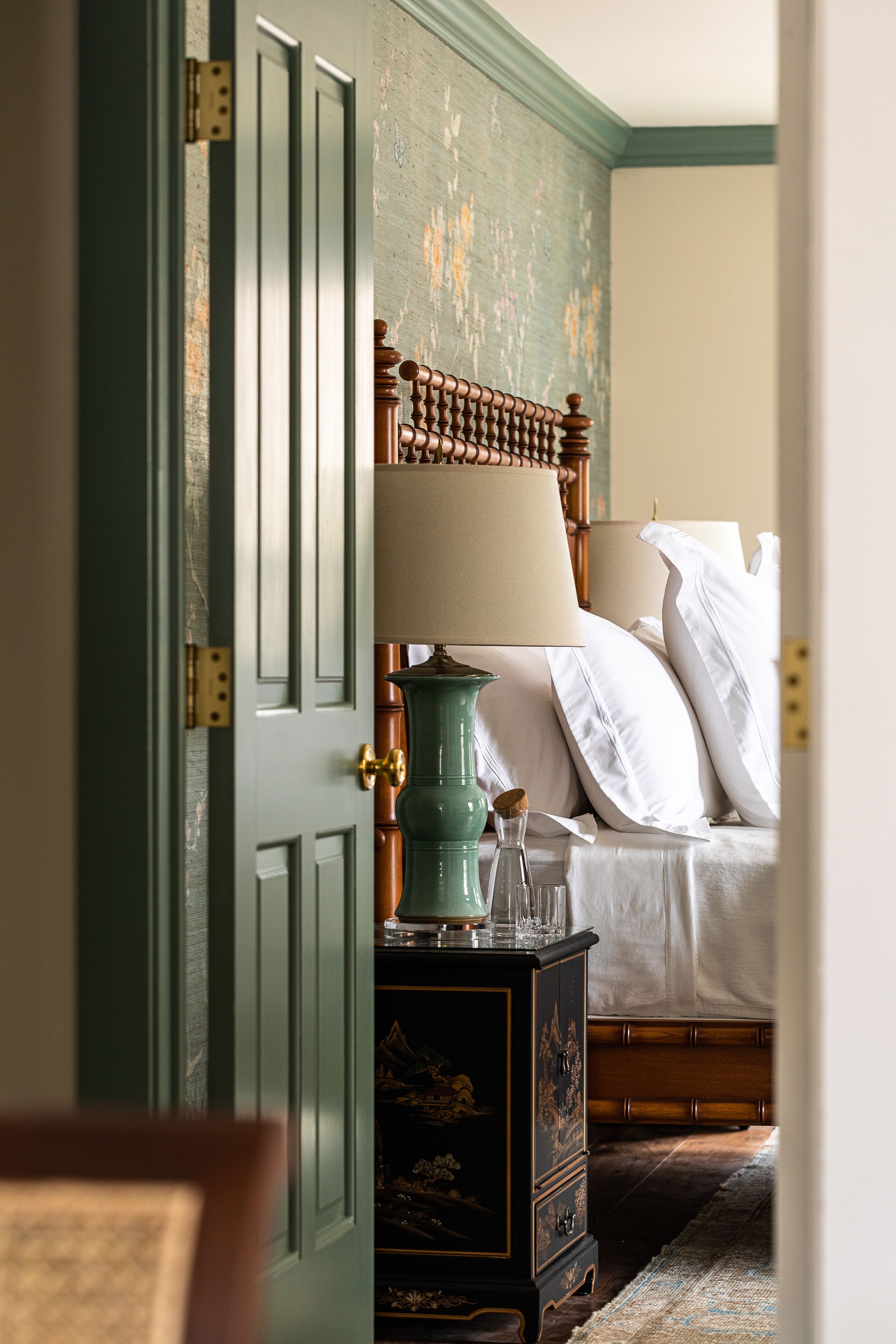 A bedroom with a wooden bed, a green nightstand, and a door with a brass handle.
