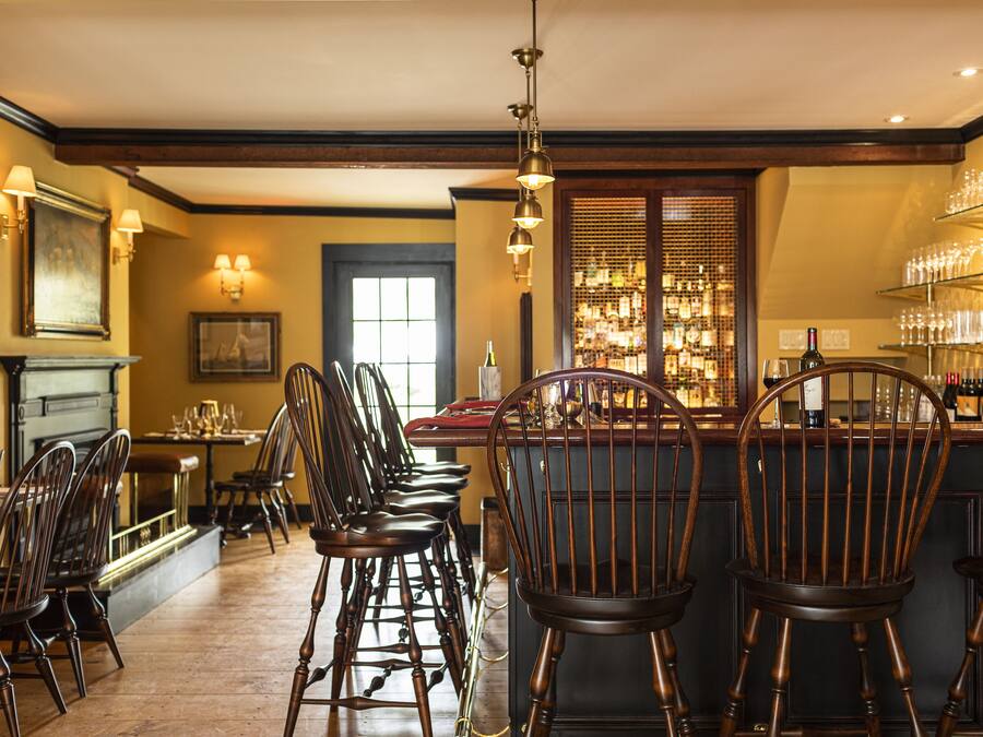 Uma área de bar com cadeiras de madeira, balcão e prateleiras cheias de copos.