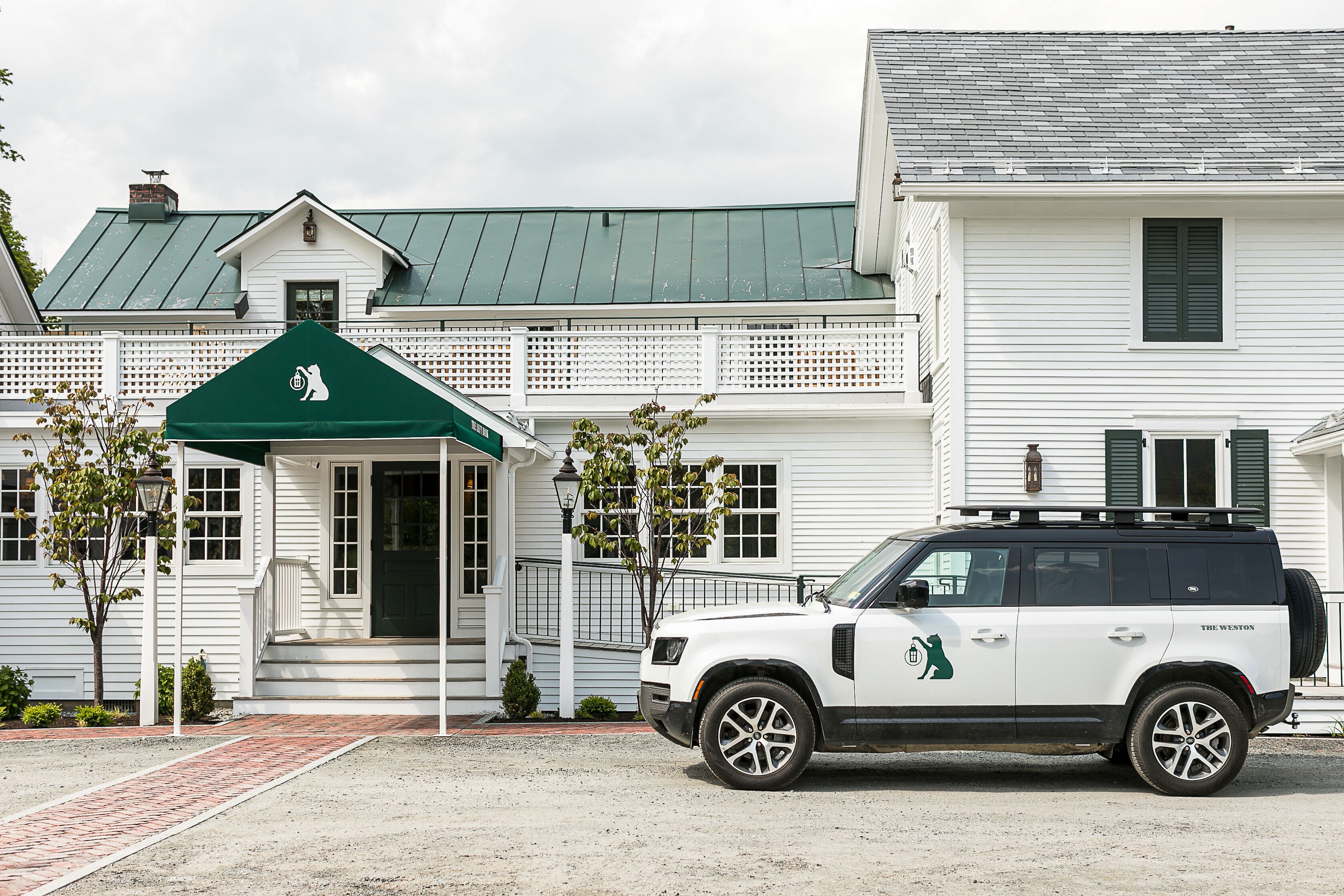 A white SUV parked in front of a white building with a green awning and a sign with a cat logo.