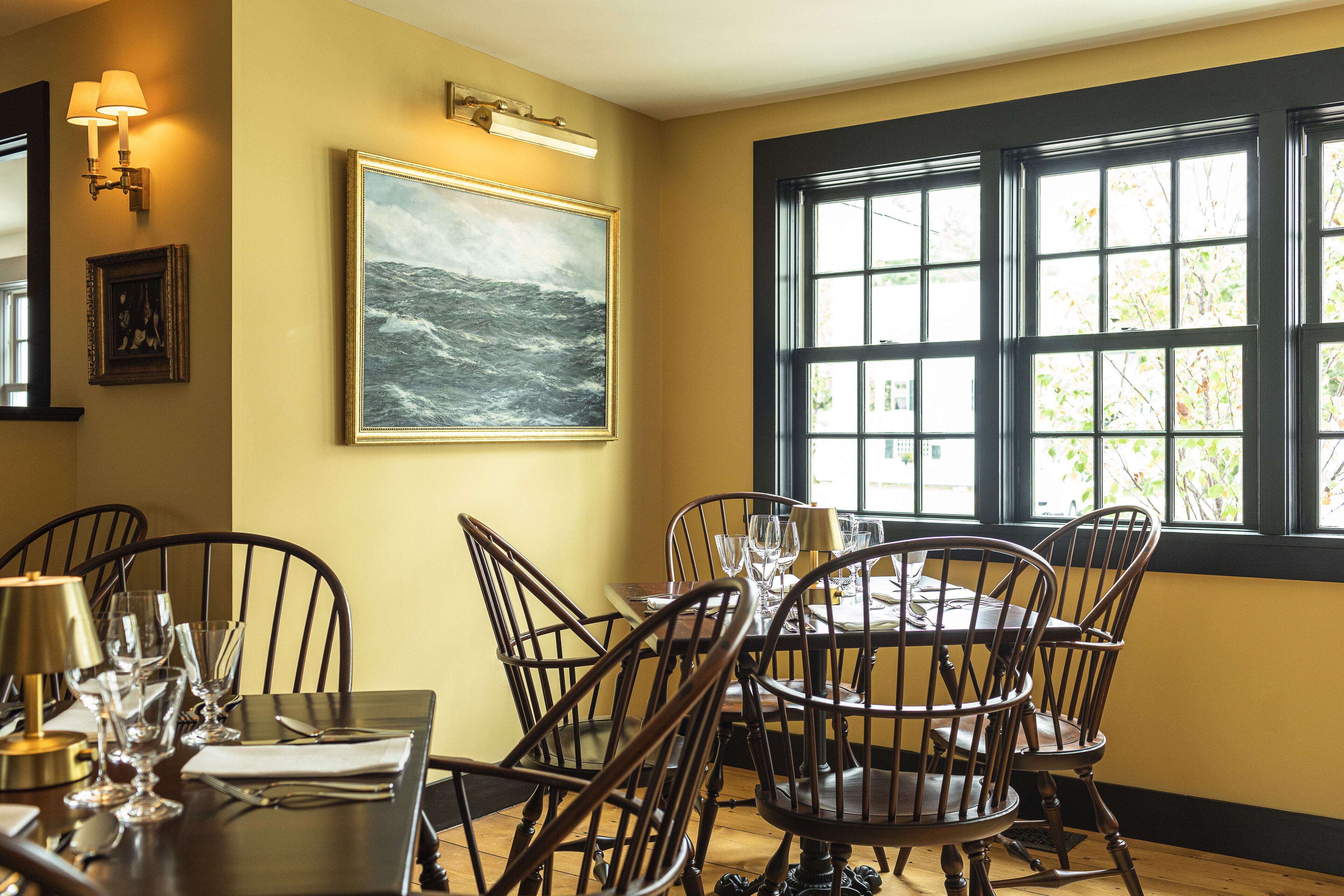 A dining area with a round table, chairs, and a painting of a stormy sea.