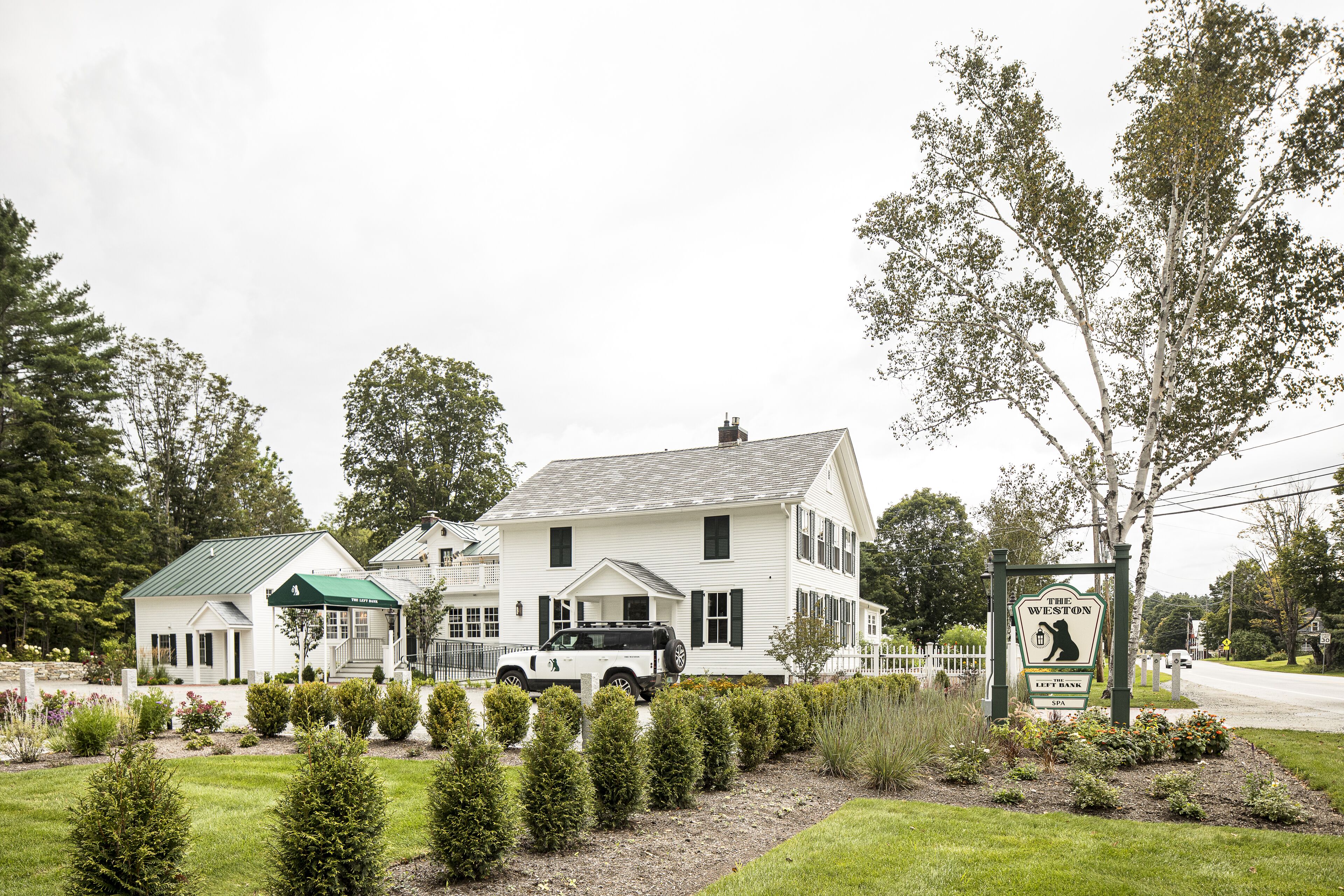 A white two-story building with a green awning, a signboard, and a vehicle parked in front.